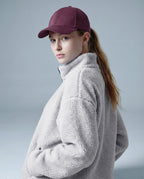 Person wearing a gray fleece jacket and maroon cap on a light gray background