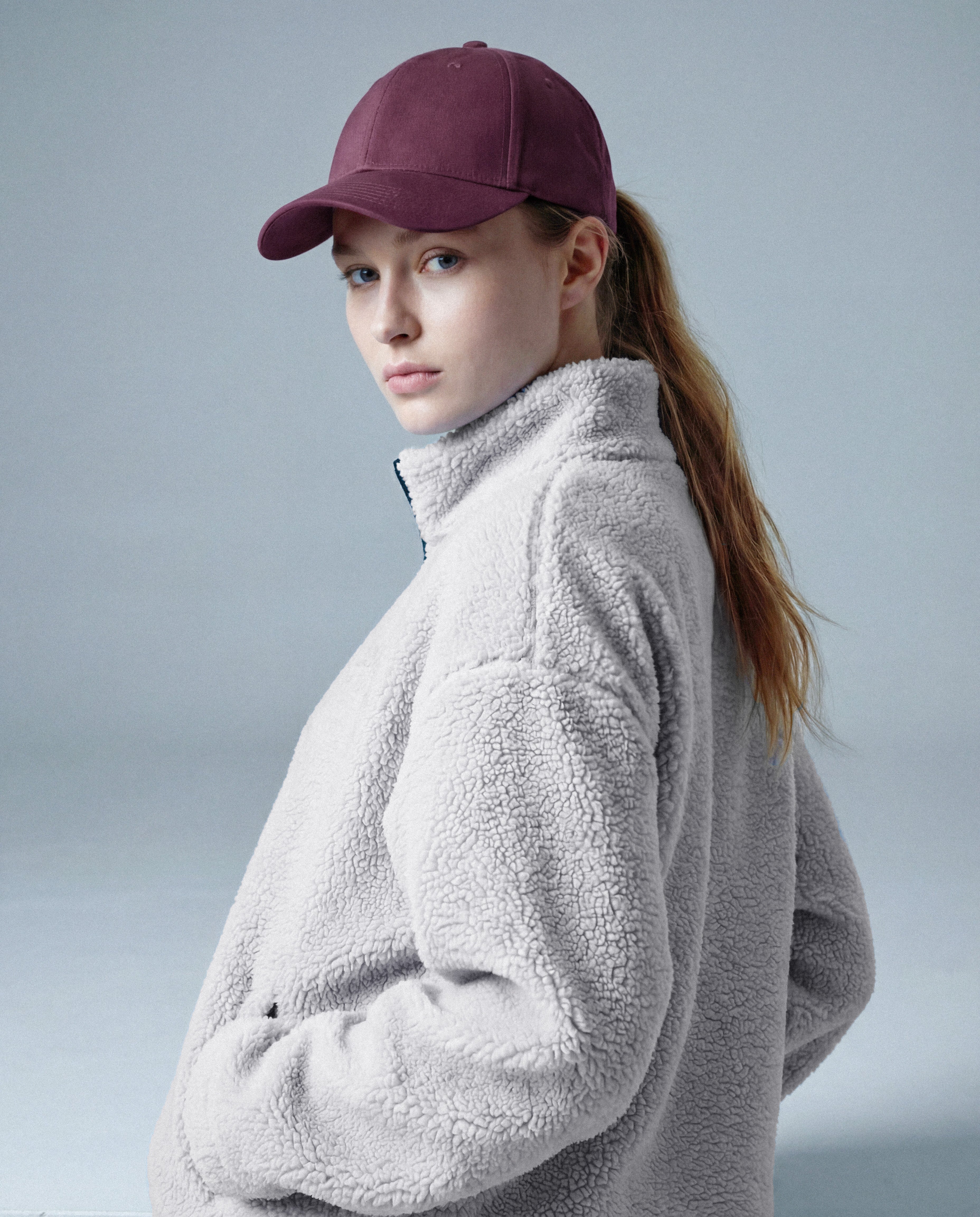Person wearing a gray fleece jacket and maroon cap on a light gray background